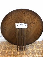 Photo of a round wooden tabletop with four detached legs placed on it. A label with #24 is visible, indicating lot number.