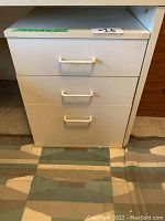Front view of small white metal file cabinet with three drawers and white handles.