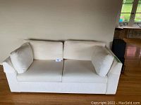 Front view of ivory fabric sofa with 2 seat cushions, 2 back cushions, and 2 armrest cushions placed on wooden floor.