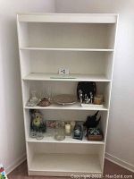 Front view of white wooden bookshelf with four shelves, displaying various decorative items which are not included.