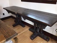 Side view of two matching antique dark wood tables highlighting carved aprons and pedestal bases.