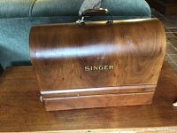 Singer wooden carrying case with curved lid and "Singer" logo on table