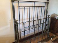 Disassembled antique brass bed frame components leaning against wall on wood floor, showing headboard, footboard, and side rails.