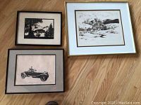 Photo showing all three framed prints together on wood floor: forest silhouette, mountain home scene, and vintage car print.