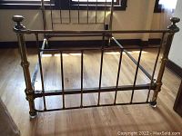 Full view of the antique brass bed frame footboard showing vertical brass rods and rounded finials.