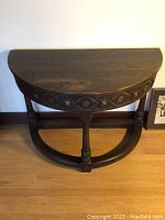 Side view of the table showing half circle carved trim on the apron and the semi-circular base platform supporting the legs