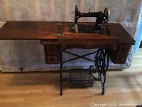 Full view of oak cabinet with fold-out extension leaf, sewing head, cast iron treadle base and drawers