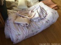 Lot of bed linens including light purple floral duvet, vintage linens, and wool blankets.