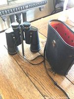 Black Harimex 10x50 binoculars sitting on a wooden surface next to a black carrying case with an orange interior.