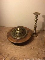 Fire pit cover on wood base with tall brass candlestick on floor against wall.