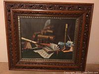 Front view of the ornate carved wood and plastic frame surrounding the still life print featuring books, music sheets, a flute, and candlestick.