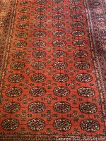 Close-up showing burnt orange field with black medallion pattern and fringe wear.