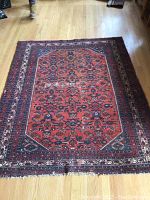 Full view of a rectangular vintage Persian area rug with a red-orange center medallion pattern and intricate borders showing frayed edges and wear.