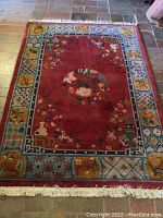 Full view of the rectangular red rug with decorative border placed on stone floor