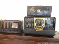 Photo of two black vintage radios side-by-side on wooden surface showing different sizes and designs.