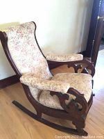 Side angle showing the full rocker base, floral fabric upholstery, and wooden carvings.