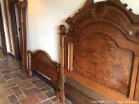 Full view of the cherry wood bed frame parts including headboard, footboard, and side rails leaning against wall.