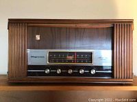 Front view showing wood cabinet, silver tuner face, control knobs and fluted columns