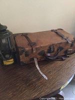 Photo of vintage leather suitcase and U.S. military lantern on wooden table