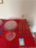 Full view of glass barware set including platters, glasses, and decanter on red cloth