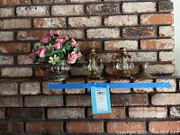 Full view of shelf with pair of Empire candle holders and faux flower arrangement against a brick wall.