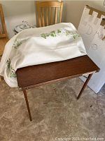 Card table with table cloth partially covering the top, two matching wooden dining chairs behind table.