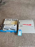 Photo of the Smith Corona XE1950 electric typewriter and the boxed three-channel wireless intercom system side by side on carpet flooring.