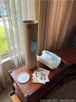 Packaging tube on side table along with two floral art prints and a COA envelope.