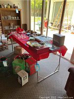 Folding camp table set up indoors with red tablecloth and various items on top, showing overall size and condition.