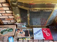 Overview of boxed Desktop Golf Shots game, Parcheesi, Sequence, Deluxe Uno, Scrabble, playing cards and Tenzi as shown on floor by fireplace.