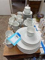 Multiple stacked plates, cups, creamer, and lidded sugar bowl arranged on a table showing the full lot.