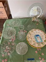 Top view of multiple clear glass platters and bowls along with two ceramic egg plates on a green cloth.