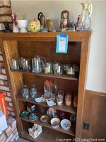 Wide view of wooden shelving unit holding multiple clear glass mugs, steins, figurines, nesting dolls, and decorative glass and ceramic items.