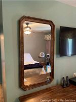 Front-facing view of the framed mirror mounted on a green wall, showing the medium brown beveled wooden frame and clear reflection.