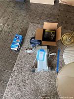 Photo showing the seated pedal exerciser, box containing Forte Courier pedal set, blood pressure kit, and blue measuring tape on carpet.