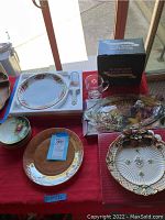 Fire King plate with floral border, German plates, Fitz and Floyd Blossom platter, Williams Sonoma Woodland Deer mug in box, and matching platter with utensil on red tablecloth
