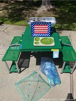 Green portable folding picnic table with attached benches, serving trays, aluminum pans on top, and bug cover beside it