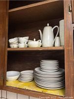 Two wooden shelves showing the Royalton china set including coffee pot, cups, sugar bowl, creamer, bowls, and plates stacked neatly.