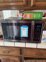 Full front view of Sharp Carousel microwave with box on top showing size reference and auction tag.