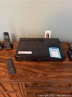 Sony DVD/VHS combo player on wooden table with remote control beside it, front and top view included.