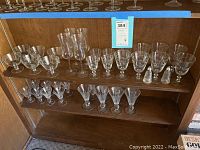 Multiple clear glass stemware pieces including tall champagne flutes, small cocktail glasses, and wider bowl glasses. Two clear glass salt and pepper shakers with metal tops shown on middle shelf.