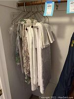 Photo showing several white and floral patterned tablecloths and napkins hanging on metal hangers inside a closet or storage space.