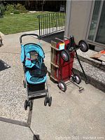 Photo showing side view of red Radio Flyer wagon upright and blue Pet Gear dog stroller upright on concrete patio area outdoors.