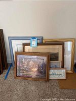 Framed wall art pieces leaning against a wall, showing variety of frame styles and sizes with visible artwork.