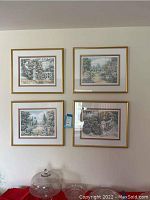 Four framed art prints with garden scenes displayed on a wall in gold frames with white and burgundy matting.