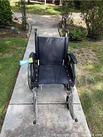 Front view of folding wheelchair showing black fabric seat and backrest, padded armrests, and metal frame.