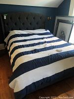Full view of king size bed frame with padded fabric headboard in dark gray, bed made with a blue and white striped comforter