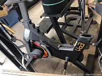 Side view of black stationary bike frame showing missing seat area and a pedal with cage strap on the left side.