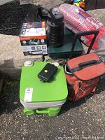 Full lot with camp stove, water jug, green/white camp toilet, soft cooler bag, and pack of red plastic cups