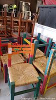Photo showing six wooden chairs with brightly painted frames in multiple colors and woven rattan seats arranged together, highlighting the colorful geometric patterns and visible wear with scratches.